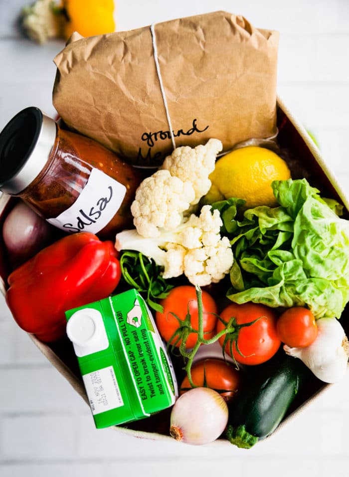 A box filled with fresh produce, pantry items, and brown paper wrapped ground beef.