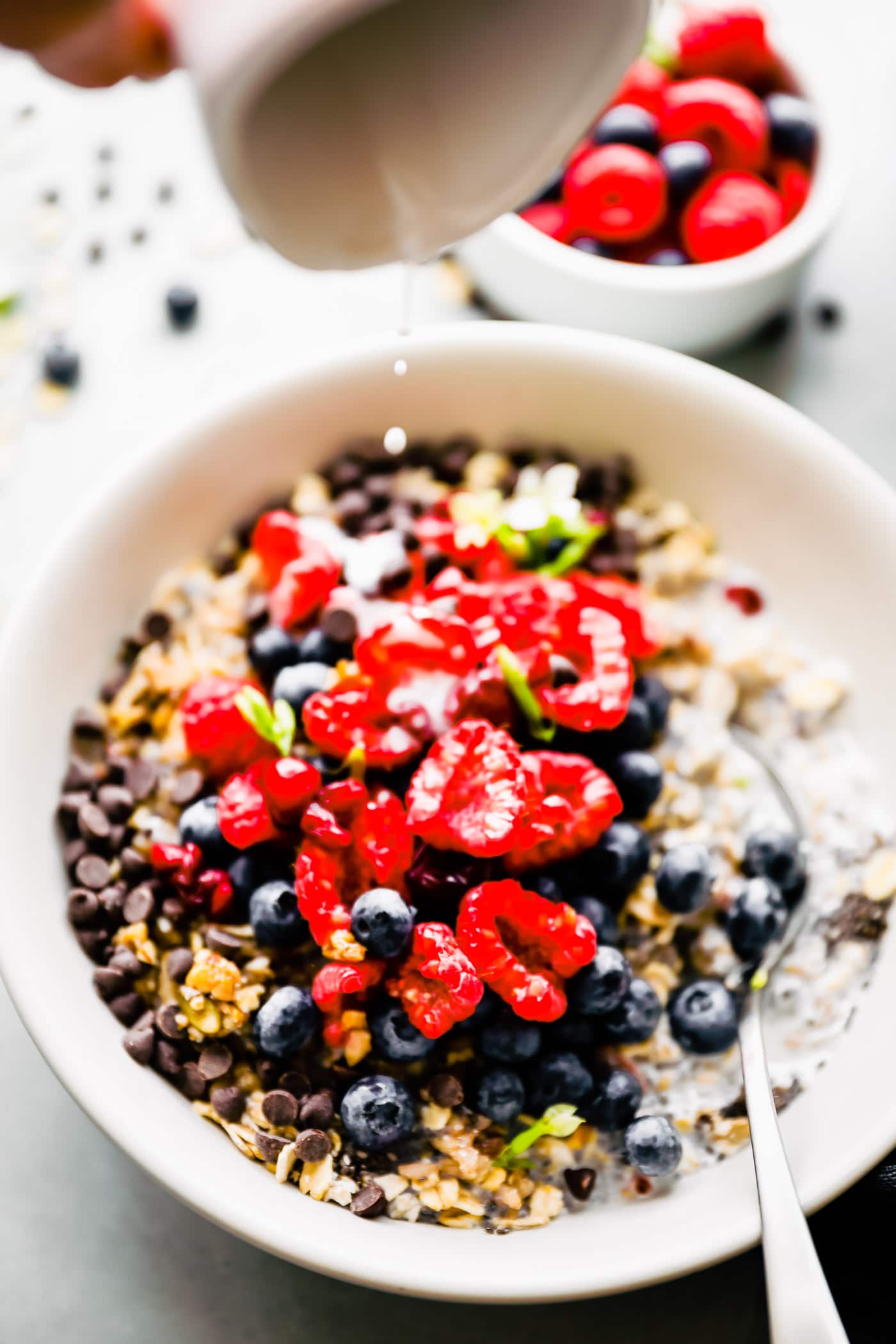 Close up overhead view fresh berries and chocolate chips over a bowl of oats, quinoa, and chia seeds.