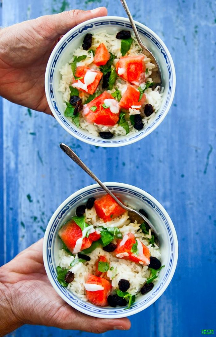 coconut rice and watermelon salad bowls being held, spoon in bowls.