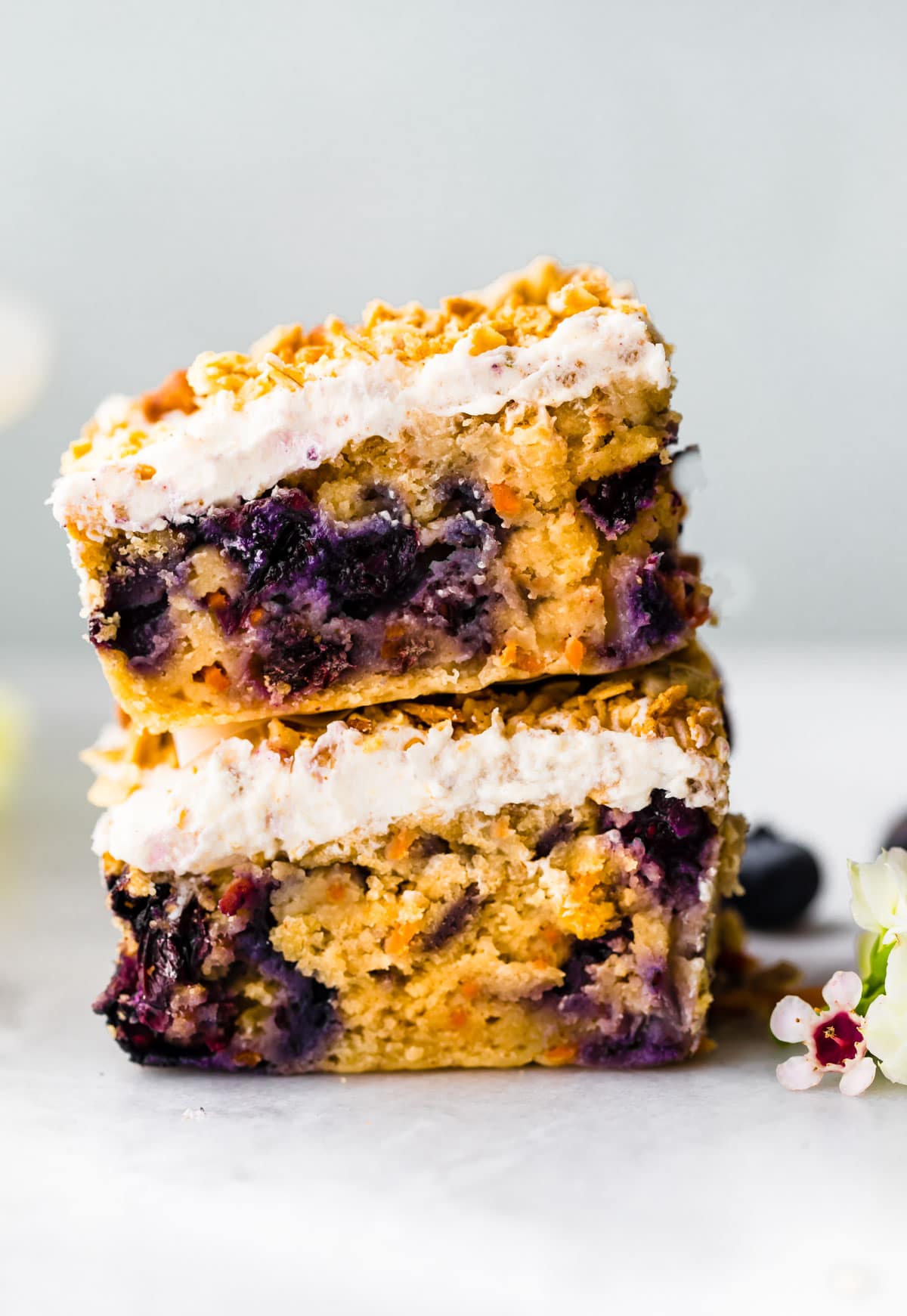 carrot cake bars with frosting and granola sprinkled on top stacked three bars high on counter