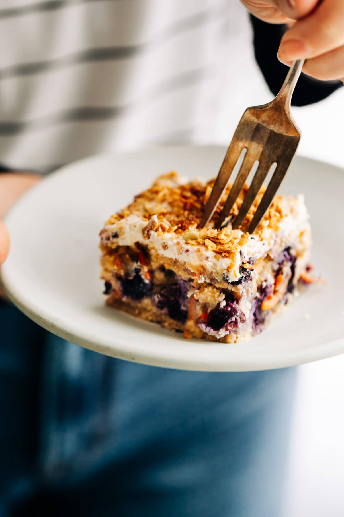 Blueberry carrot cake bar on plate with frosting and granola sprinkled on top.