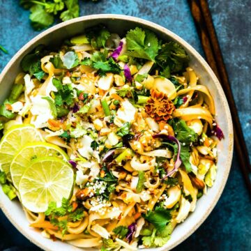 Spicy Thai rice noodle salad in bowl topped with nuts, sauce, and lime slices.