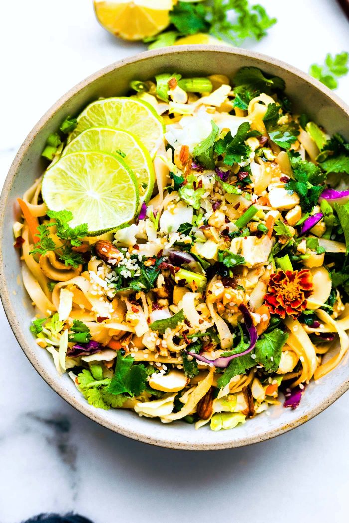 Close up view spicy Thai rice noodle salad in bowl topped with sesame seeds and lime slices.