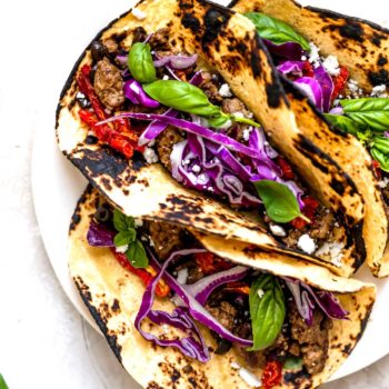 Three lamb tacos served in charred tortillas topped with purple cabbage