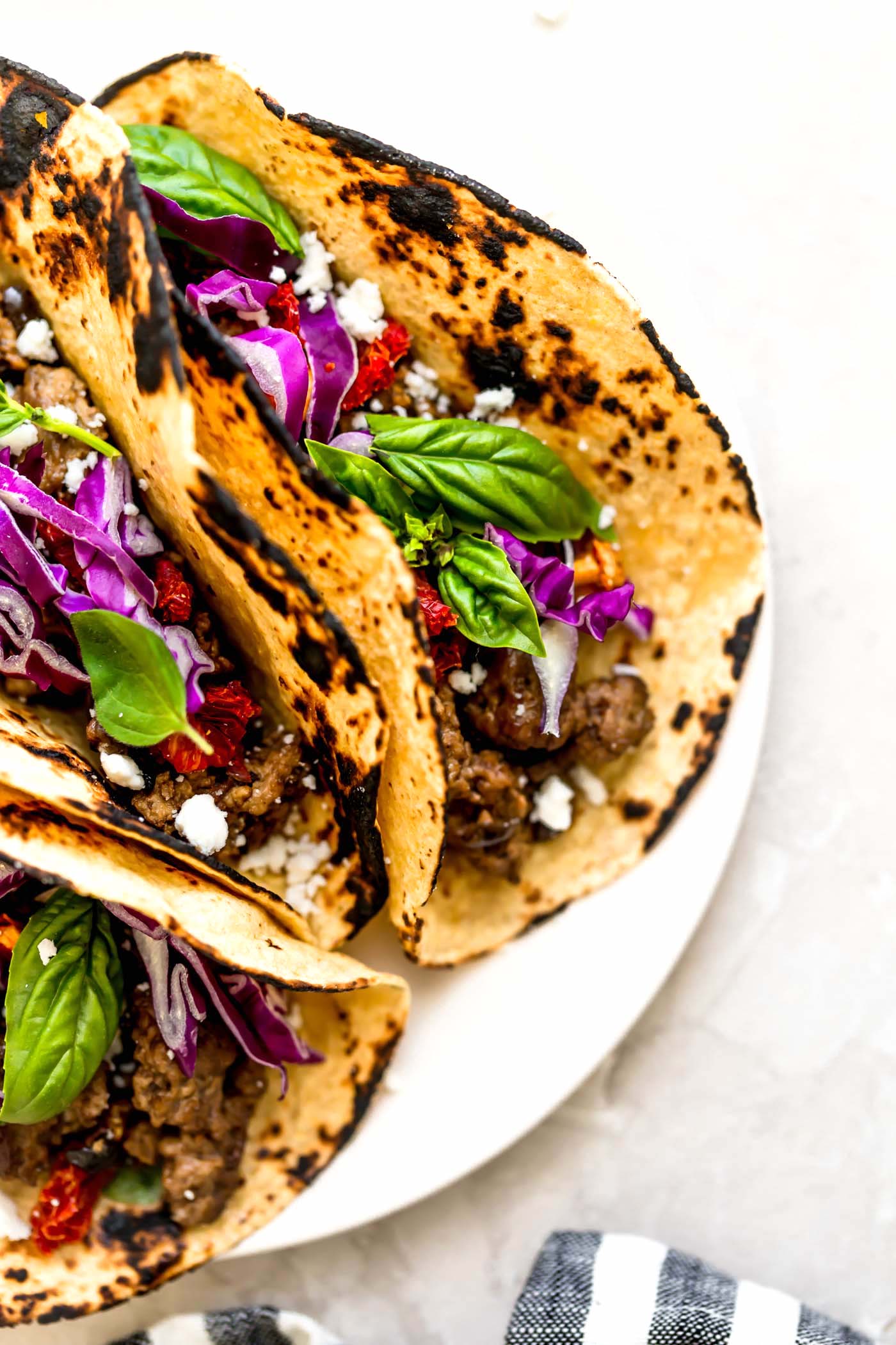 Greek lamb tacos in charred tortillas with purple cabbage and fresh herbs on top