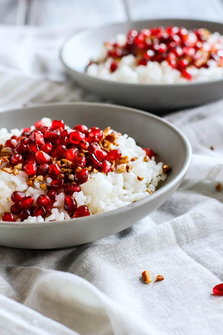 Coconut Rice and Pomegranate Porridge! A nourishing gluten free breakfast bowl made with jasmine rice, coconut milk or cream, cinnamon, maple syrup, nuts, and cinnamon. We call this the performance carb porridge because of the budget friendly jasmine rice which makes great fuel when combined with other nutrient dense foods!