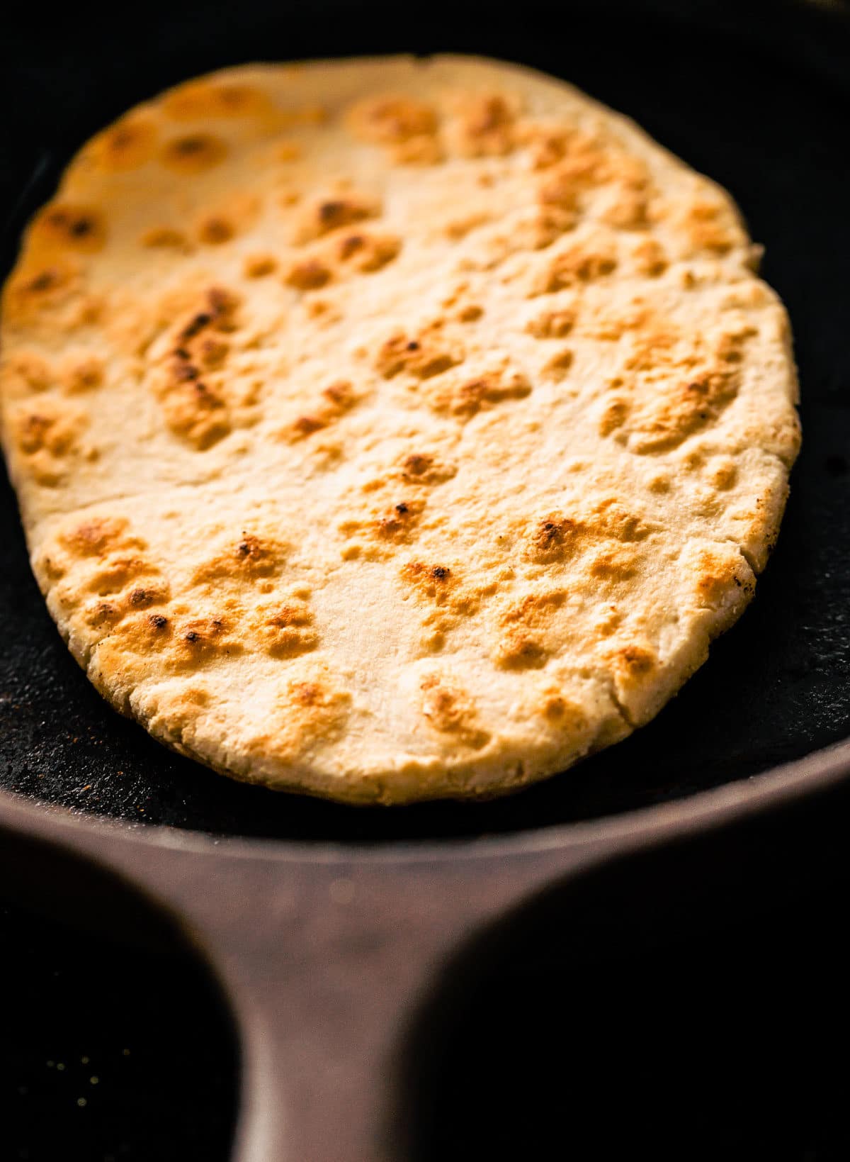 A lightly browned naan bread in skillet over black stovetop.