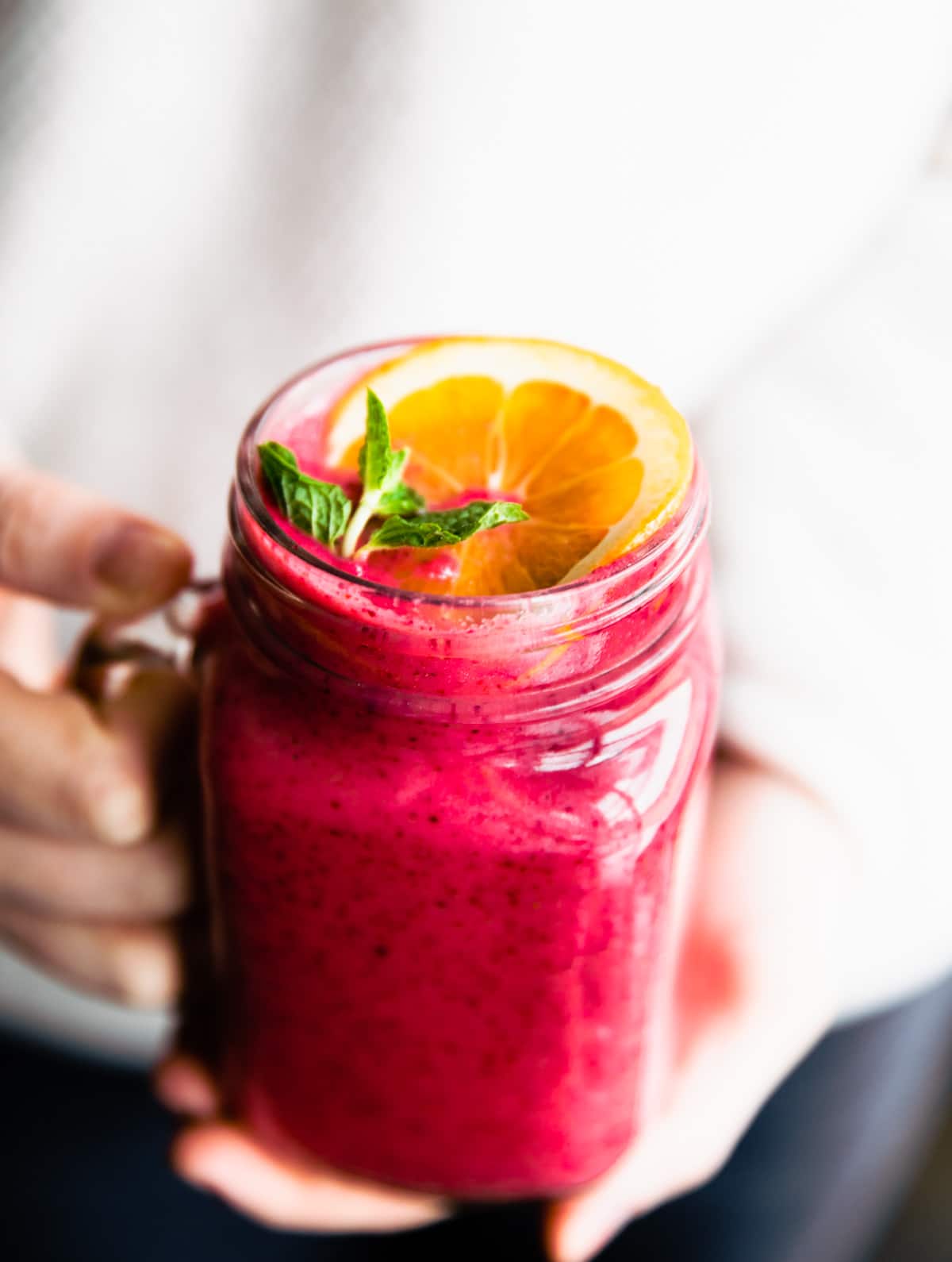 A hand holding a glass cup with handle filled with bright pink immunity boosting frozen fruit smoothie