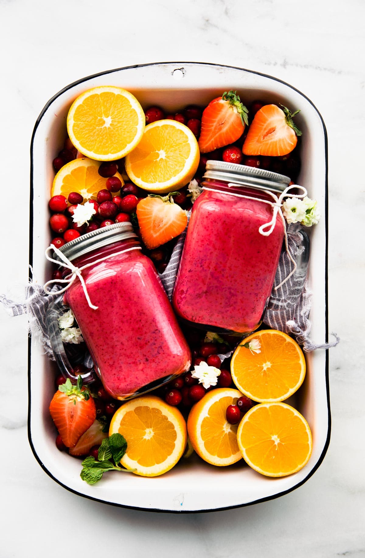 Overhead view white metal tray filled with fresh fruit and two mason jars filled with immunity boosting frozen fruit smoothie.