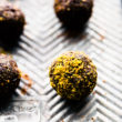 A row of chocolate pistachio protein bites coated in crushed pistachios lined up on baking sheet.