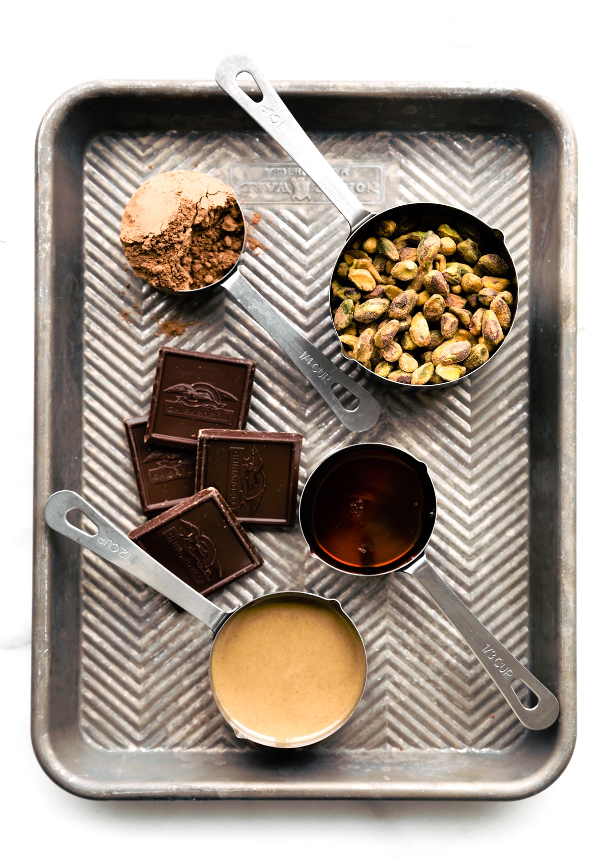 All ingredients for chocolate pistachio protein balls in baking dish in measuring cups.