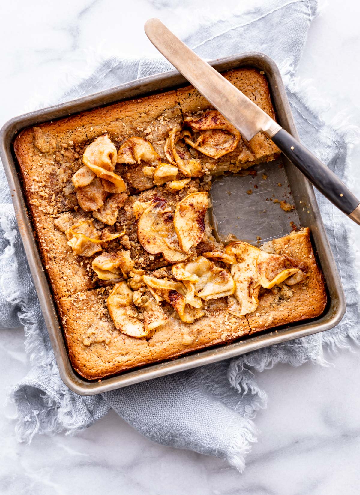 Apple coffee cake in square baking pan cut into equal squares, one square removed.