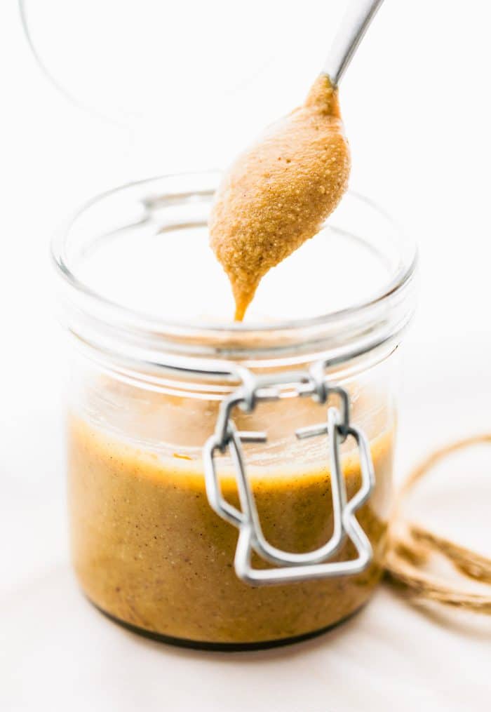 A spoonful of homemade cashew butter hovering over a jar of cashew butter.