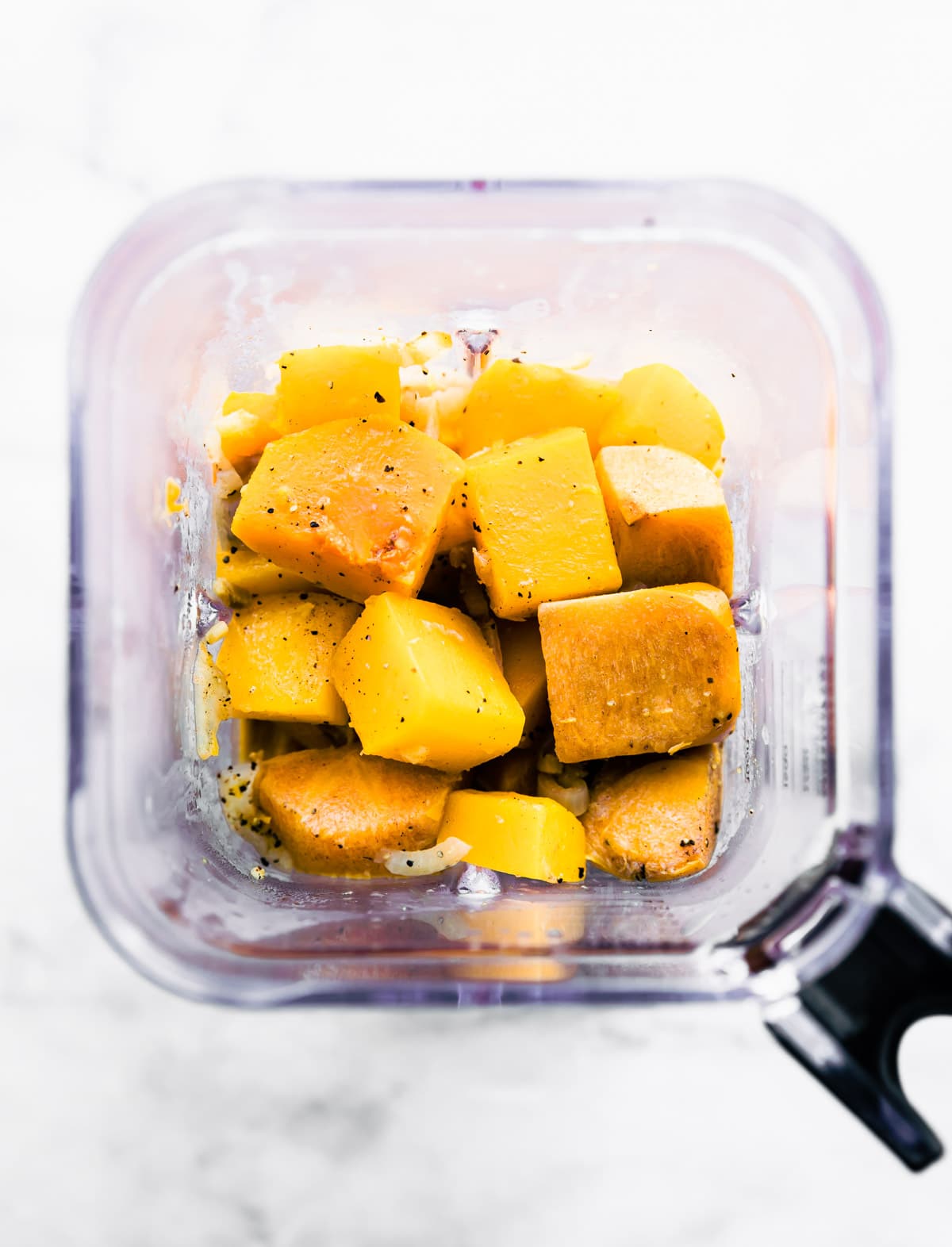 Overhead view blender cup filled with roasted butternut squash pieces