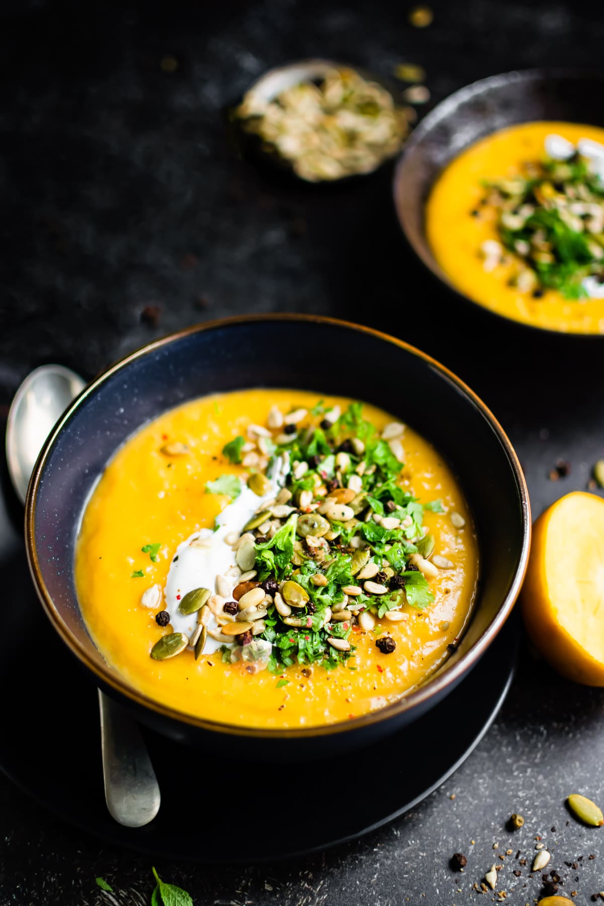A black bowl filled with roasted butternut squash soup topped with cream and seeds.