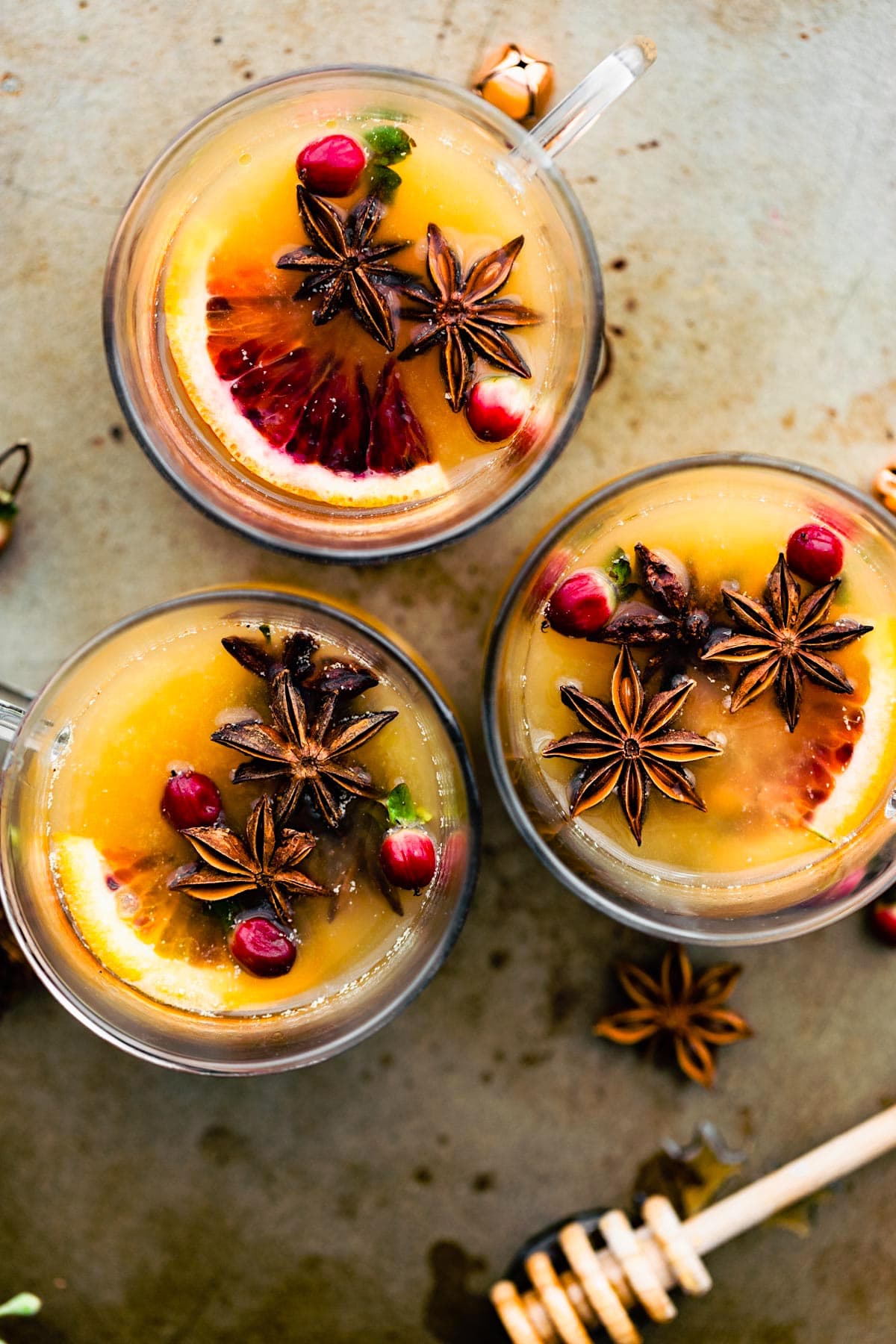 Three glasses with hot toddy with spiced rum arranged together, fresh fruit and spices floating in liquid.