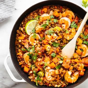 Overhead view shrimp and lentil jambalaya in a white skillet with wooden spoon