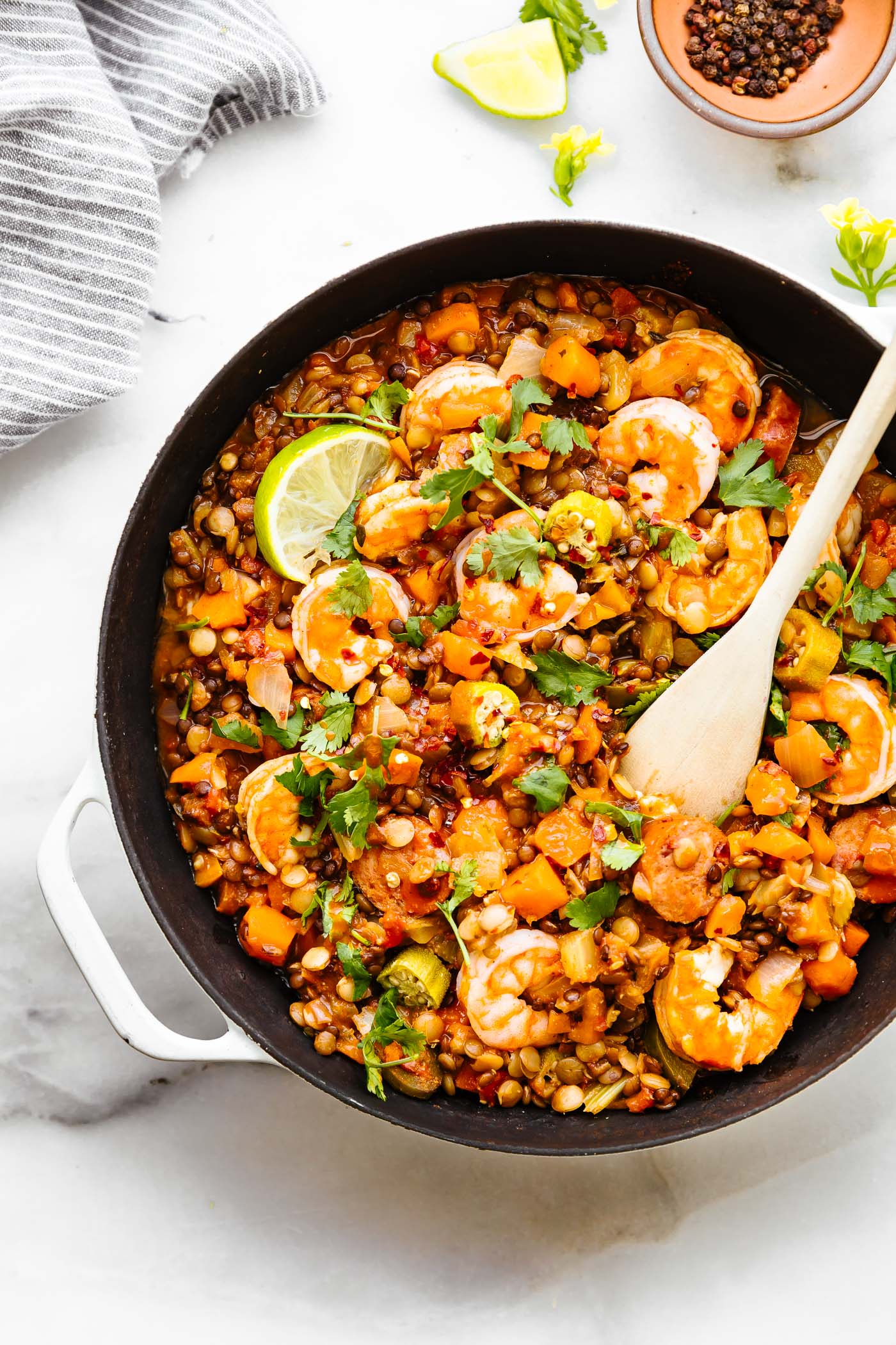 Shrimp jambalaya in a skillet topped with cooked shrimp and lime slices, wooden serving spoon in jambalaya.