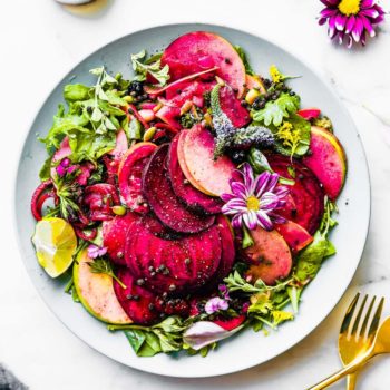 Marinated beets and apples over mixed greens on blue plate.