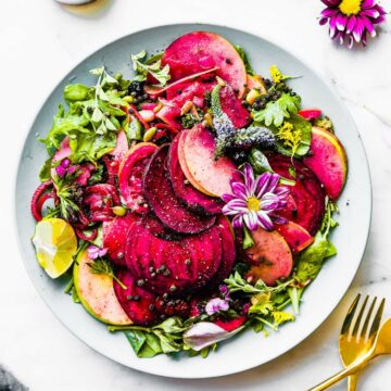 Marinated beets and apples over mixed greens on blue plate.