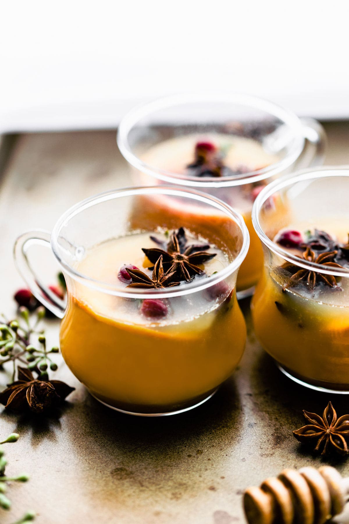 Three handled glasses filled with hot toddy spiced rum with floating cranberries and star anise.
