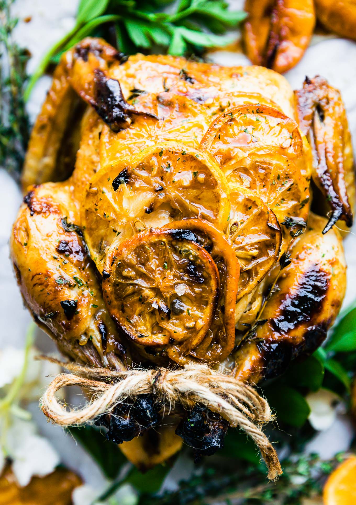 Roasted whole chicken with orange slices caramelized onto skin, chicken legs tied together with twine.