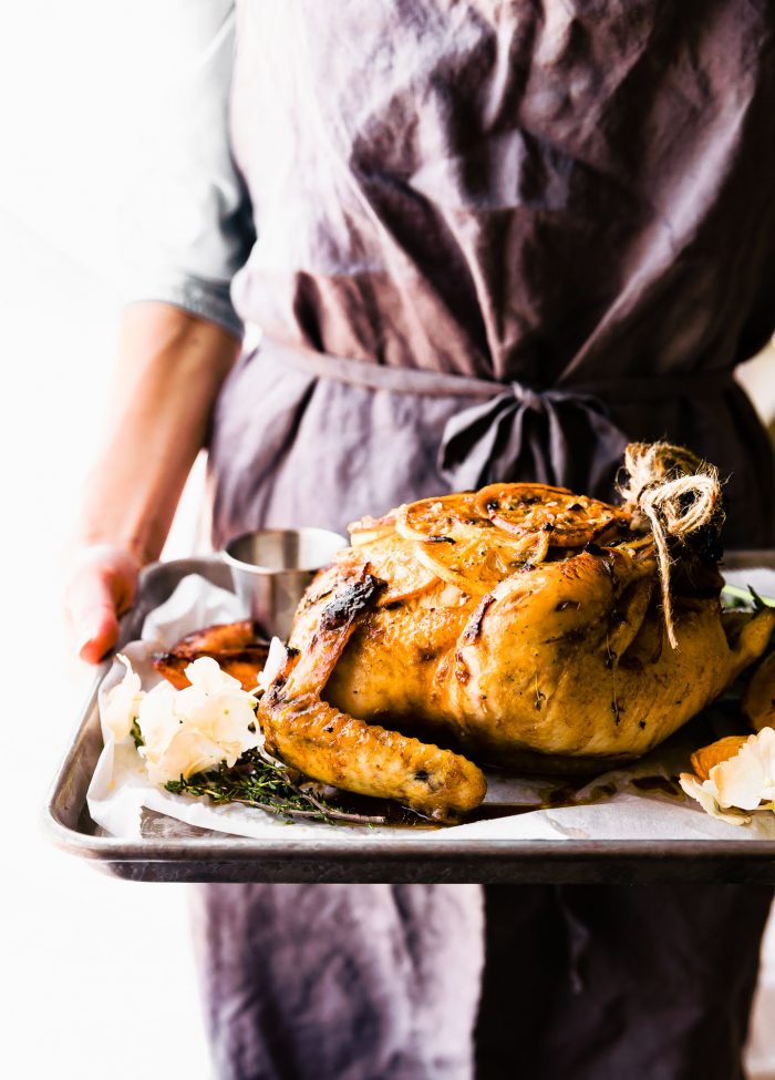 Two hands holding silver baking sheet with roasted orange honey glazed whole chicken