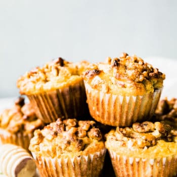 Several spiced pear muffins with nut topping stacked up in a pile on a white tray.