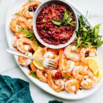 Cranberry basil shrimp cocktail dipping sauce in small bowl on white platter surrounded with shrimp