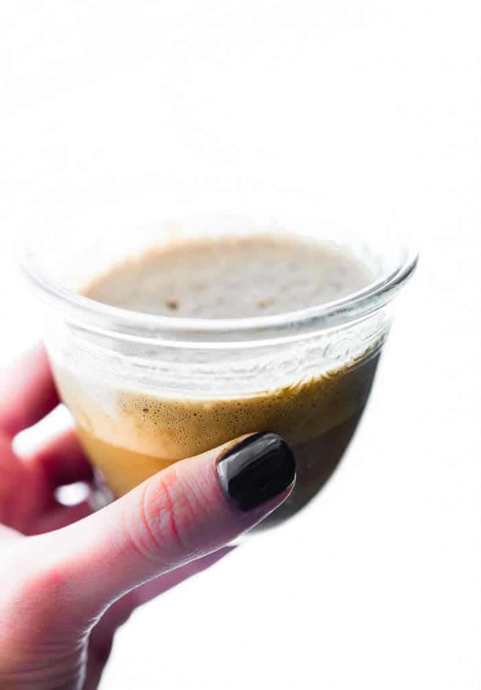 A short glass filled with coffee and cashew cream being held
