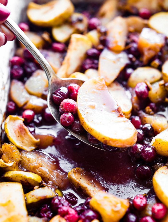 Close up view of easy spiced hot fruit bake being scooped up with a spoon, thick cut apple slices and fresh cranberries in thick sauce.