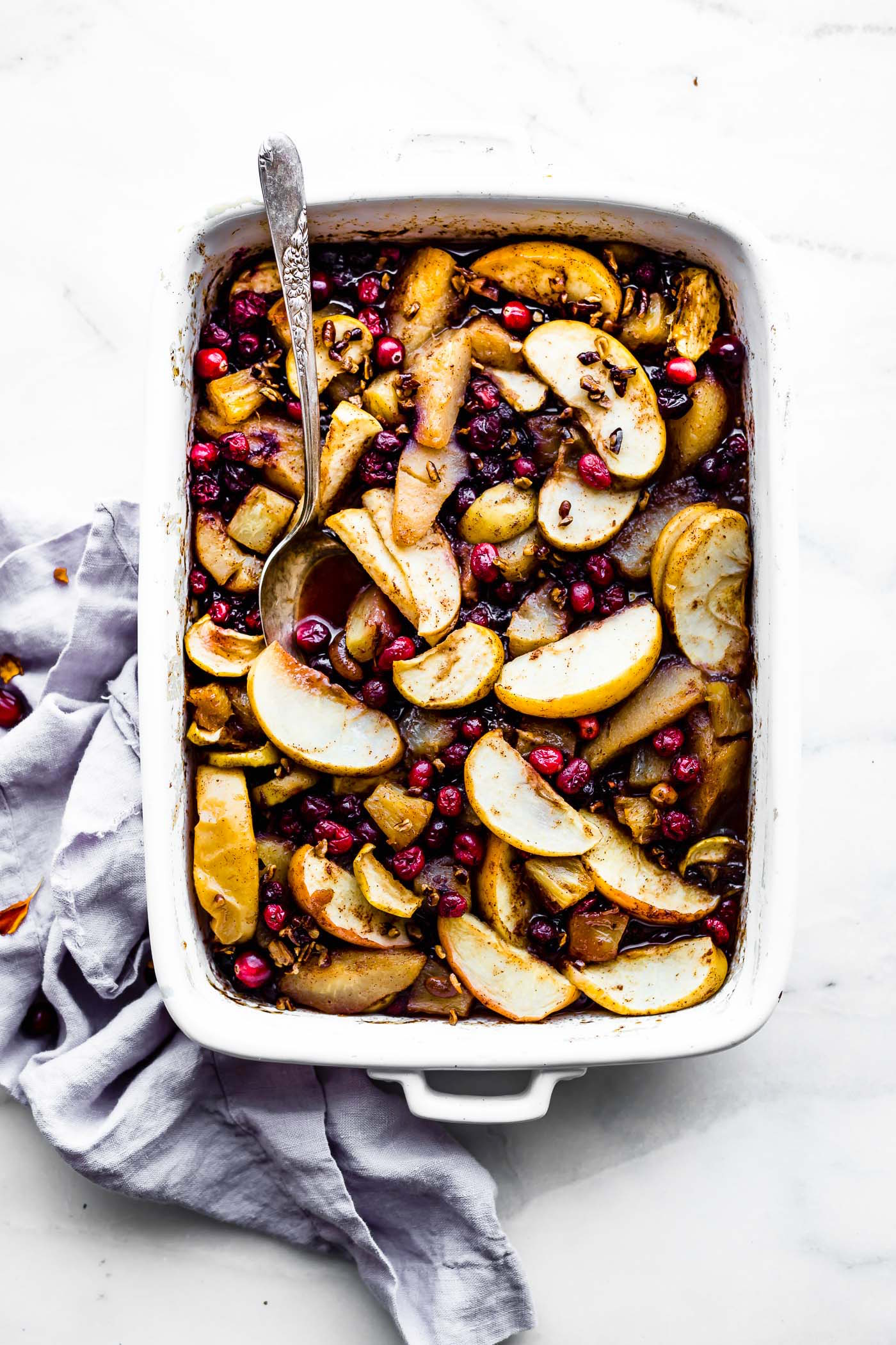 Easy spiced hot fruit bake in white casserole dish with serving spoon