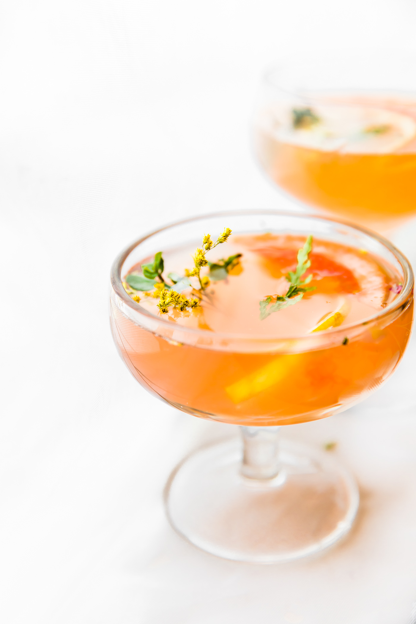 Two glasses filled with Paloma cocktail, topped with orange slices and small flowers.