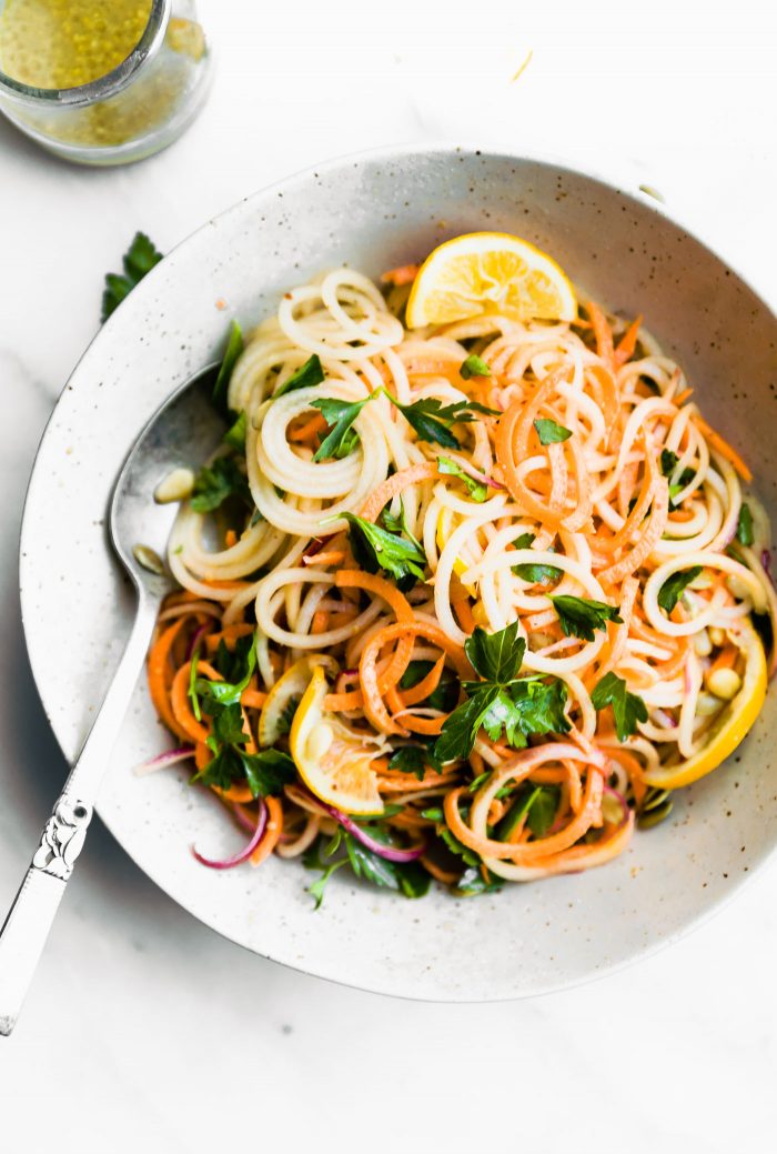 Light and Zesty Carrot Celeriac Spiralized Salad in bowl with dressing and spoon.