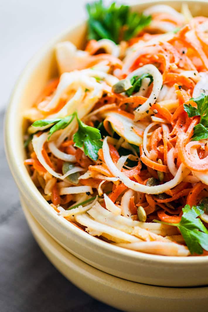 Close up view carrot and celeriac spiralized noodles with sauce in bowl.