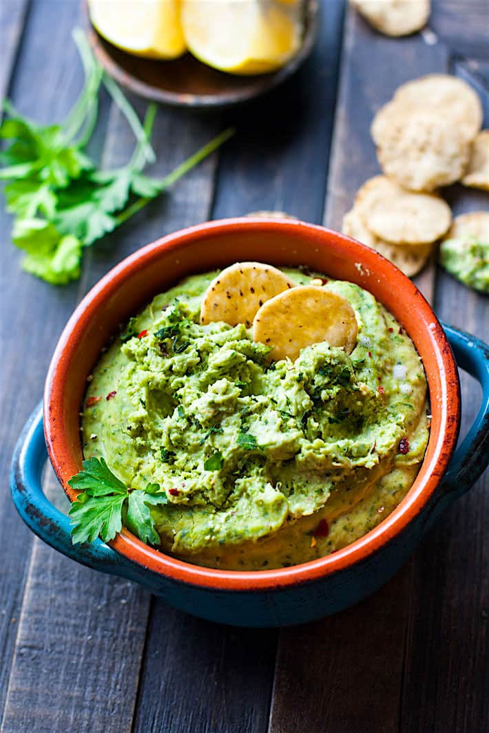 Easy Chimichurri White Bean Hummus| Green chimichurri hummus dip in an orange and blue bowl topped with crackers and fresh cilantro