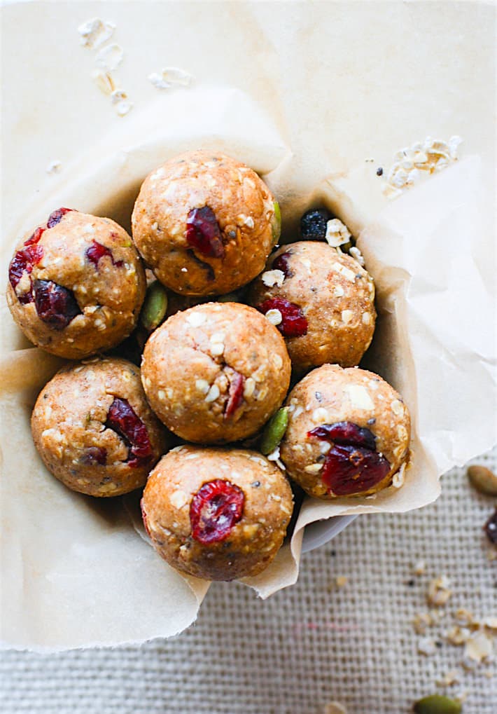 Overhead view of Muesli Energy Bites with dried cranberries and raw pepitas in each bite-size round ball; in a parchment-covered bowl.