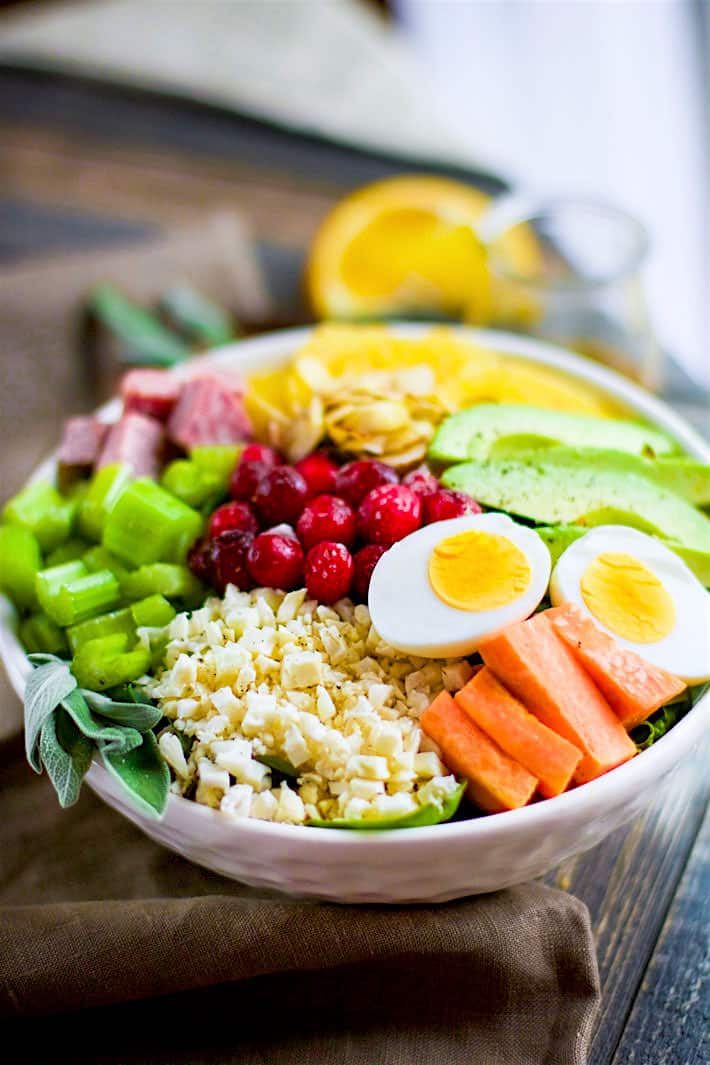 A winter-time seasonal Cobb Salad made with carrots, celery, cranberries, cauliflower rice, avocado, and more; served in a white bowl