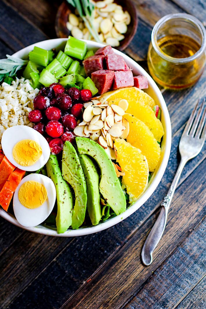 Overhead view of a seasonal Cobb Salad made with fresh fruits and vegetables with a hard boiled egg on top, served in a white bowl.