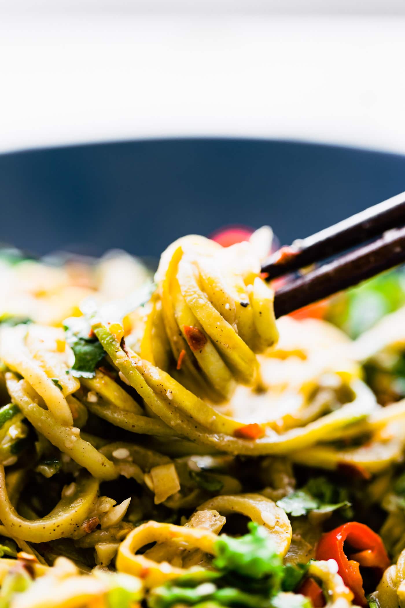 Satay style zoodles twisted on a pair of chopsticks in a bowl of spiralized satay vegetables.