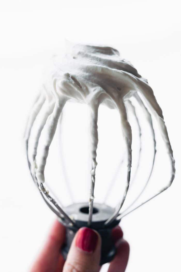 A stand mixer whisk filled with fluffy white whipped cream.