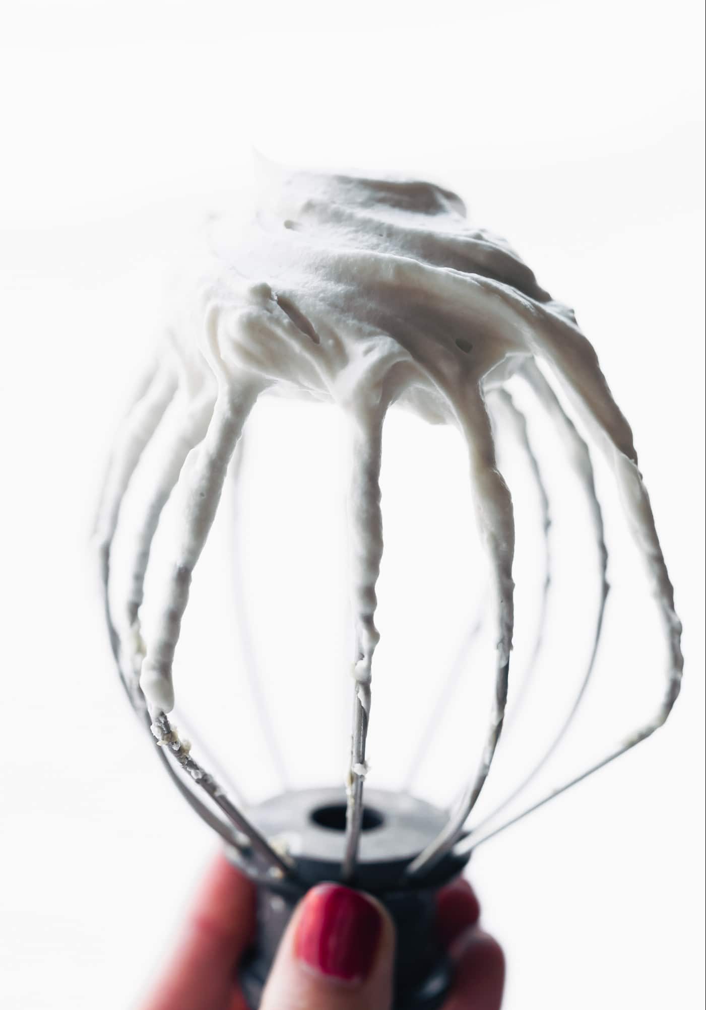 A stand mixer whisk with coconut whip cream on wires being held