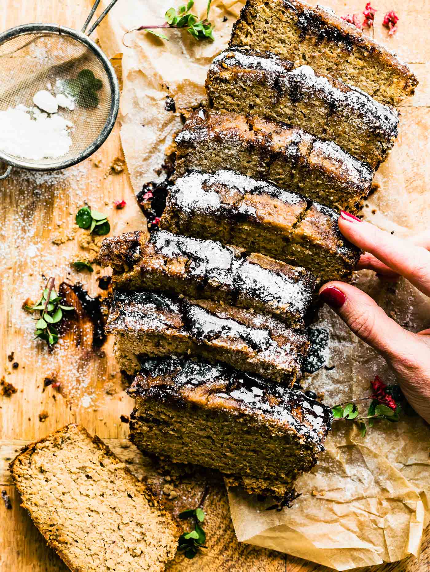 A hand removing a thick slices of Irish Cream Banana Bread from the middle of cut loaf, on a wooden cutting board.