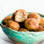 Turquoise bowl filled with cinnamon vanilla protein bites with a bite out of one ball.