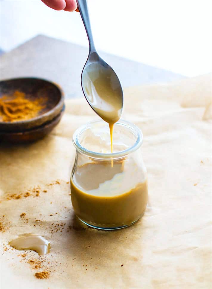 vegan dulce de leche sauce dripping from spoon into jar of the sauce