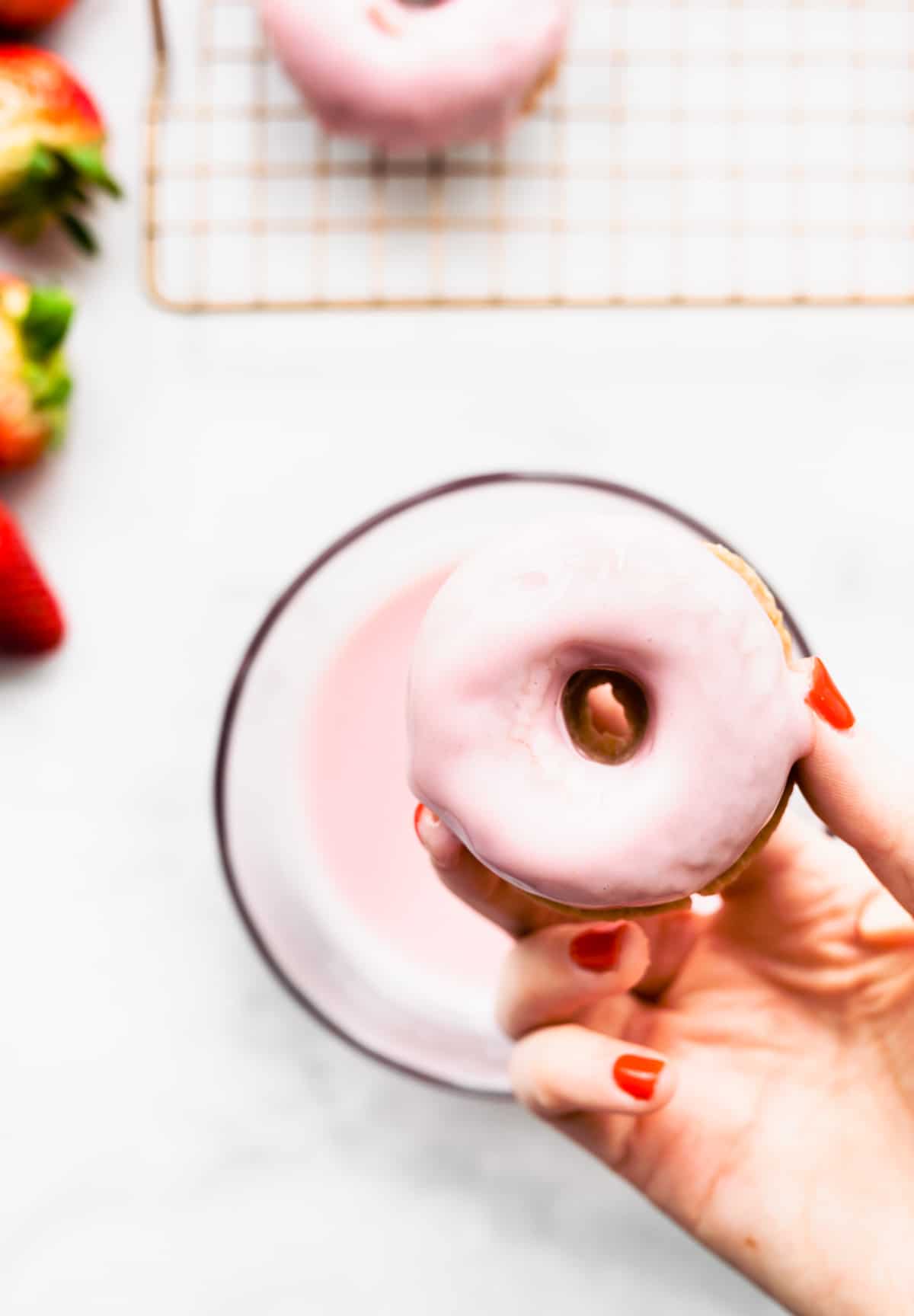 A woman's hand holding gluten free strawberry donut with strawberry yogurt glaze