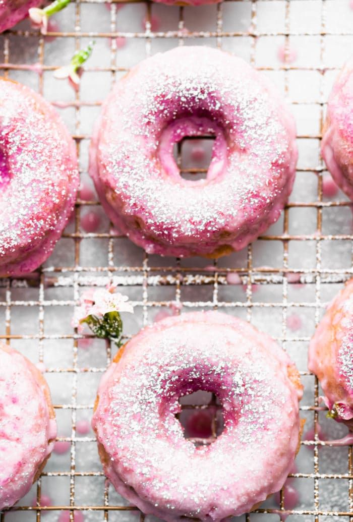 strawberry glazed donuts dusted with powdered sugar on a wire baking rack