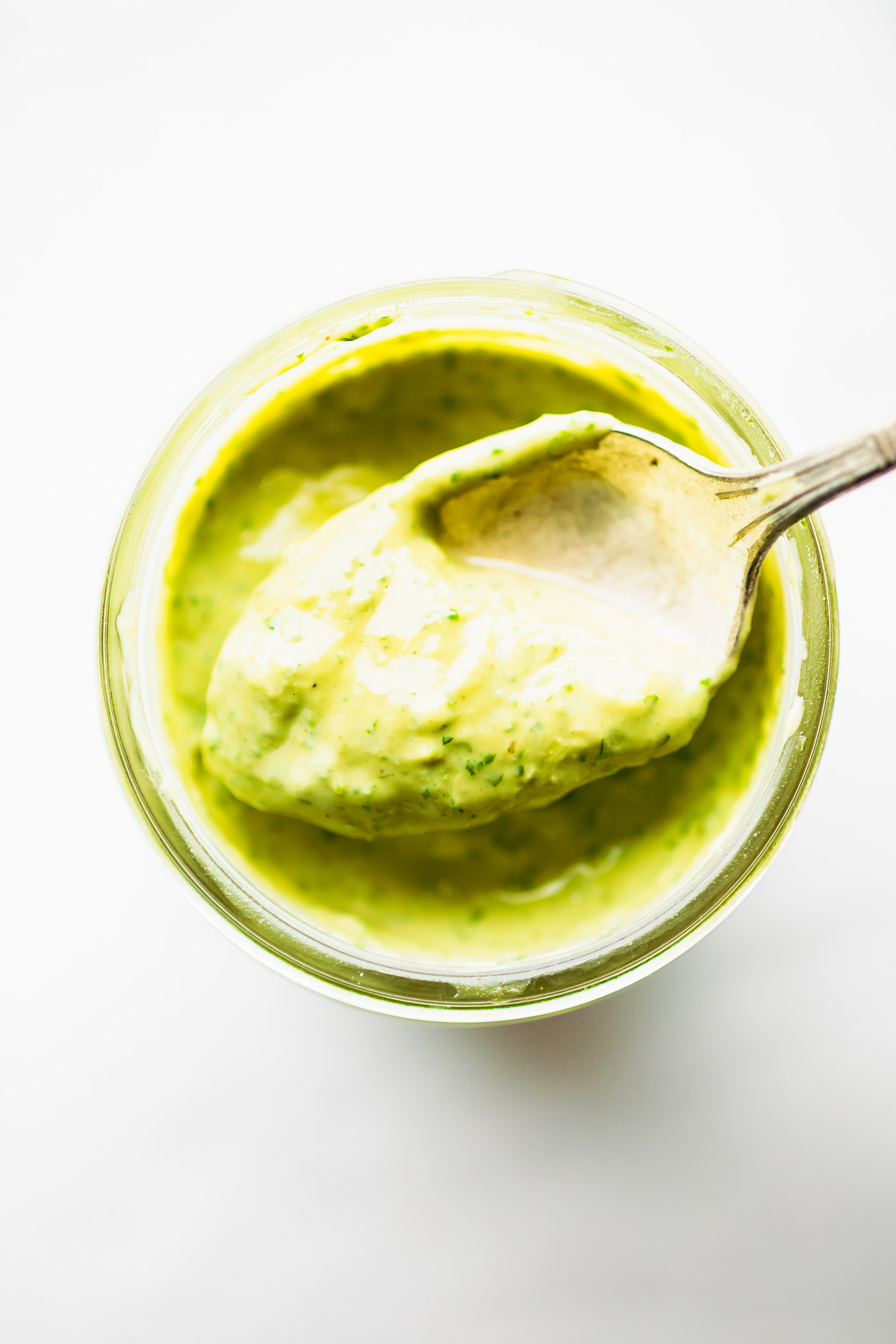 green goddess vegan dressing in a small glass jar with spoon with serving on it.