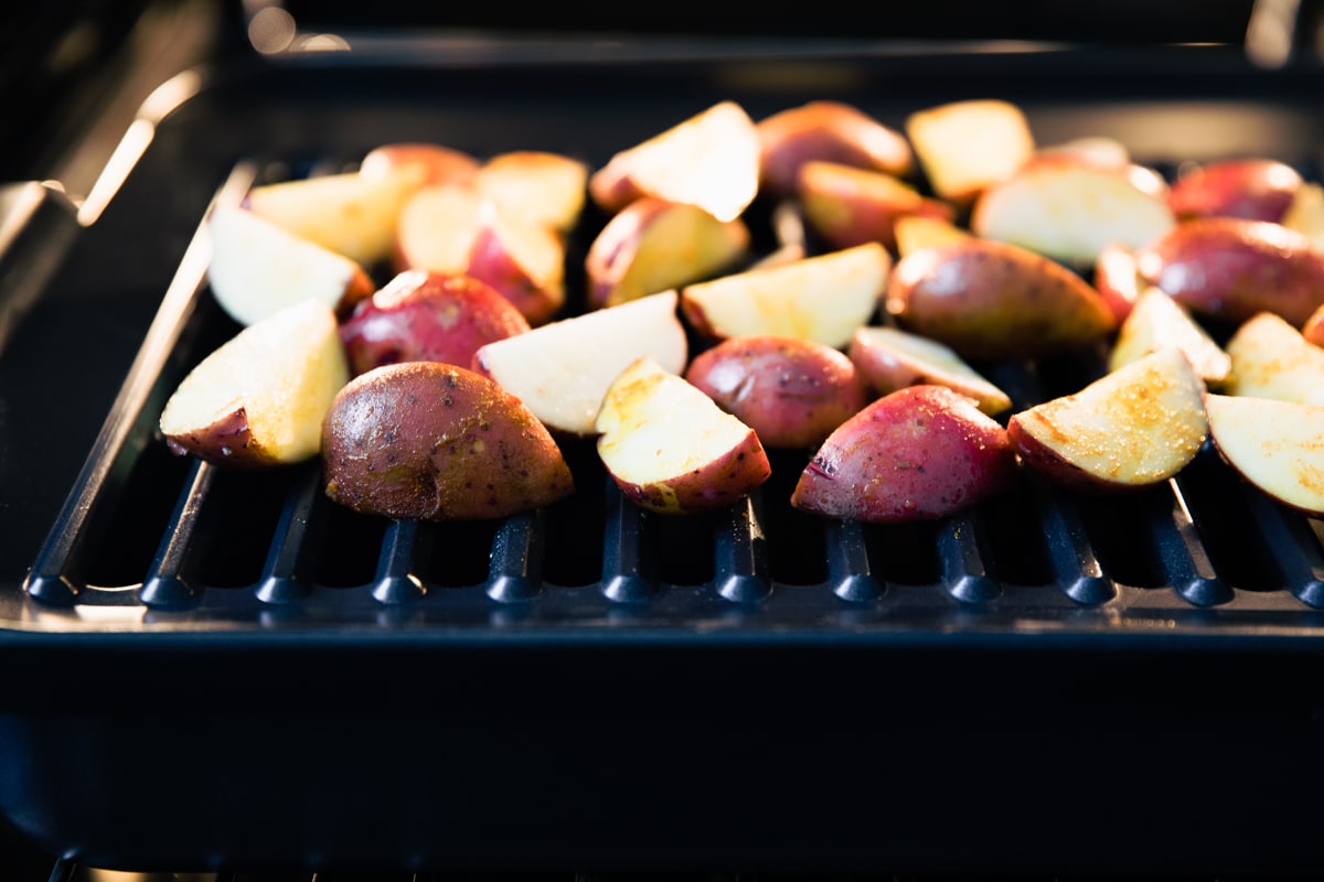 Red potato wedges on baking pan in oven