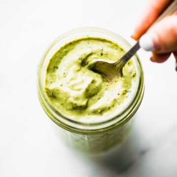 Overhead image of vegan green goddess dressing on a spoon over a mason jar